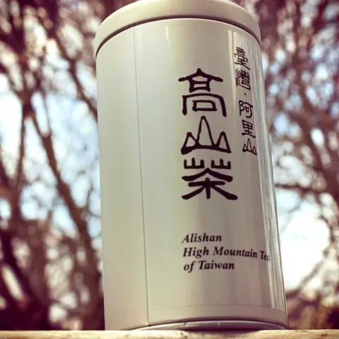 White tin labelled Alishan High Mountain Tea of Taiwan, with bare winter branches behind