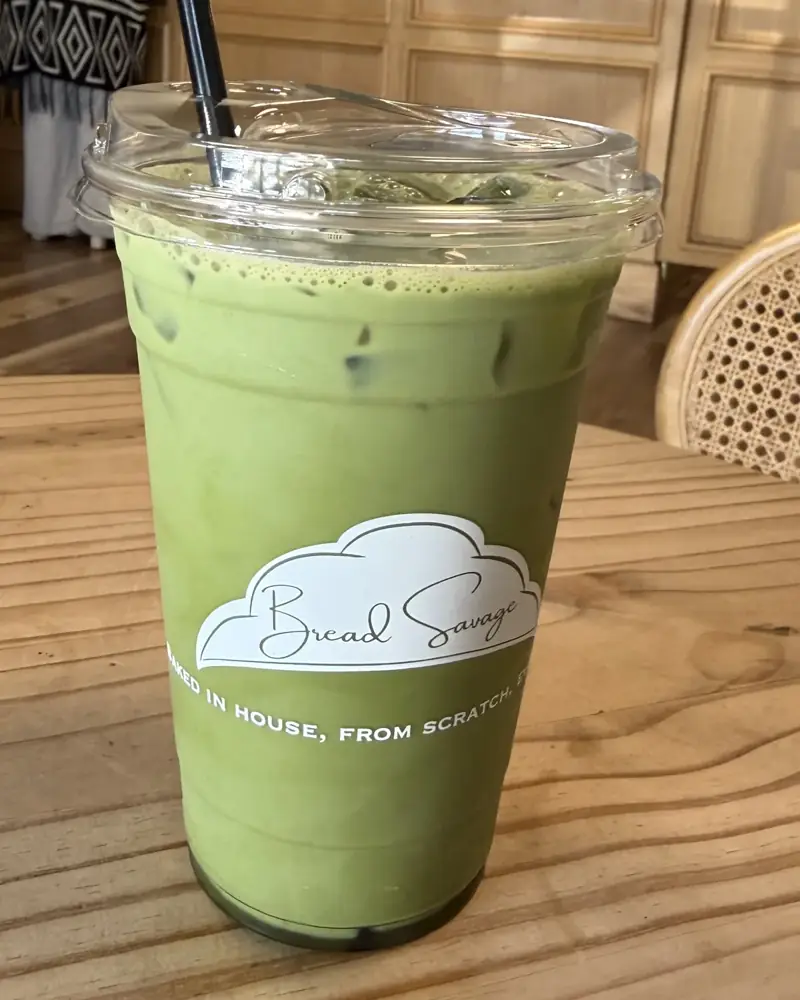 Iced matcha latte with vanilla and lavender in a Bread Savage cup on a wooden table in Visalia