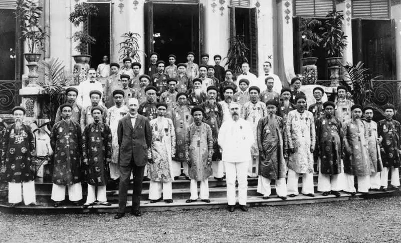 Black and white group photograph of Vietnamese mandarins in court dress and French officials at a tea of honour in Hue, 1924
