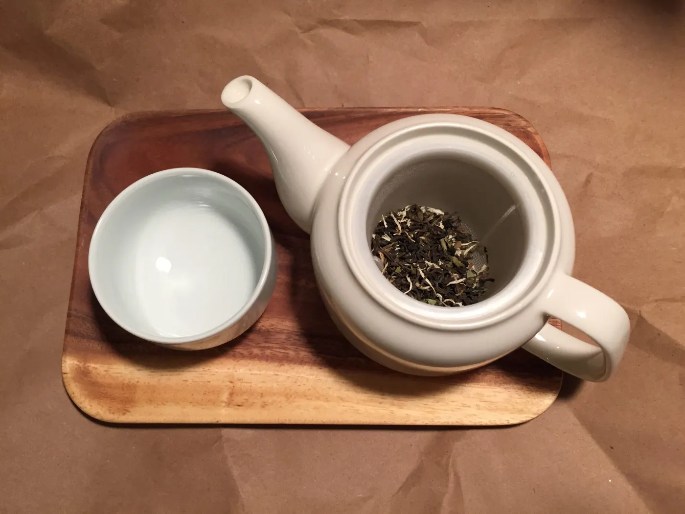 White teapot with Sacher Blend leaves and a cup on a wooden tray