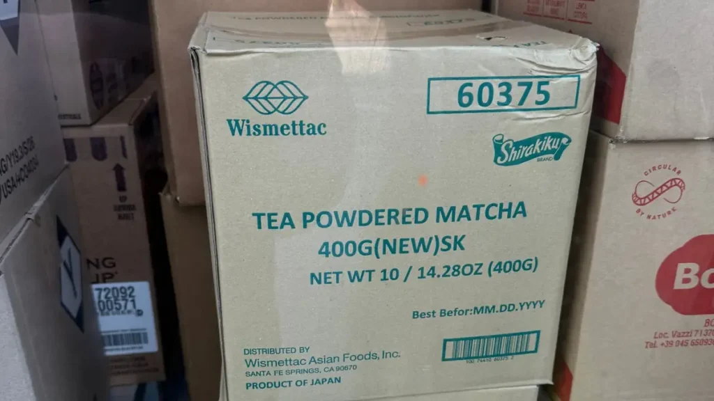 Stacked cardboard cases of powdered matcha from Japan, each holding ten 400 g bags, in a shop window