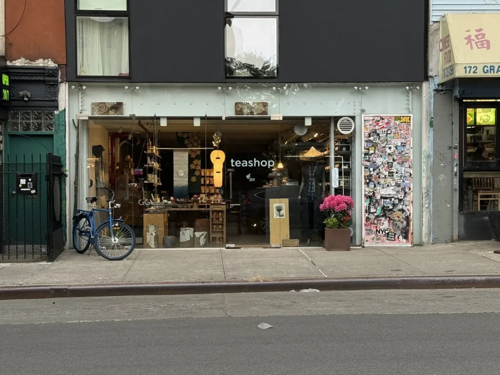 Puerh Brooklyn's glass storefront on Grand Street in Williamsburg, with a blue bicycle and pink azaleas outside